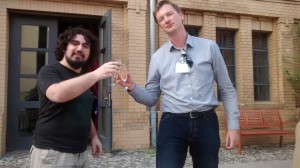 Dos personas mirando a cámara con copas en las manos, brindando.